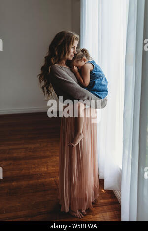 Lunghezza piena vista della madre e figlia coccole per finestre in studio Foto Stock