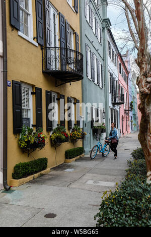 Una donna cammina la sua bici in Charleston, Carolina del Sud lungo vivacemente colorati edifici. Charleston, è la più antica e la più grande città della Carolina del Sud un Foto Stock