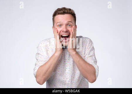 Emozionato casual uomo in piedi con le mani alzate vicino al viso Foto Stock