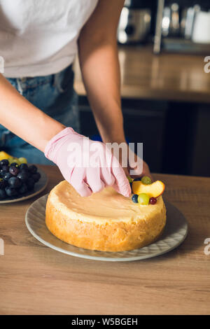 Donna con le mani in mano in rosa guanto decorare sommità di una torta con frutta Foto Stock