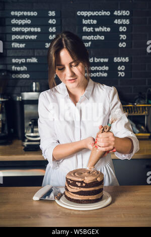 Donna con le mani in mano in camicia bianca decorare la torta al cioccolato nel cafeteri Foto Stock