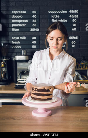 Donna con le mani in mano in camicia bianca decorare la torta al cioccolato nel cafeteri Foto Stock