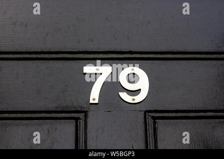 Il numero civico 79 in metallo argento cifre su un di legno nero porta anteriore Foto Stock
