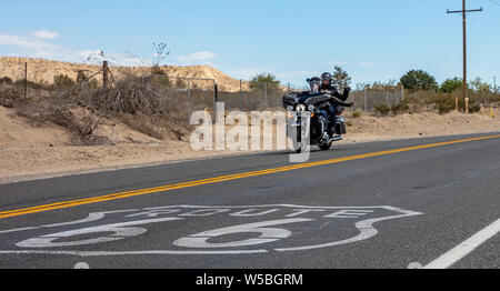 Route 66 e moto. Coppia giovane biker sventolare, in sella a una moto in una storica Route 66 highway, molla giornata soleggiata, STATI UNITI D'AMERICA. Foto Stock