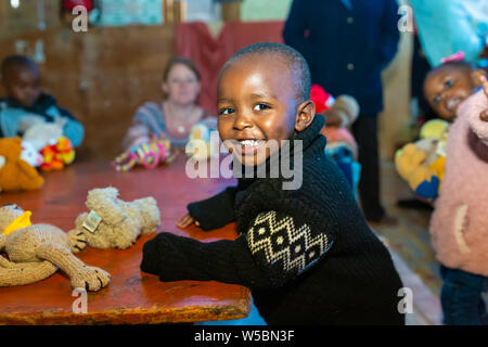 Nanyuki, contea di Laikipia, Kenya - Giugno 10th, 2019: giovani kenioti sorridente bambino seduto a tavola mentre al vivaio giocare con giocattoli imbottiti che aveva bee Foto Stock