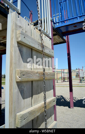 Parco giochi in legno area di arrampicata nel cortile della scuola con la scuola in background. Foto Stock