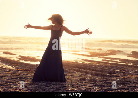 Grato donna romantica sulla spiaggia al tramonto. Foto Stock