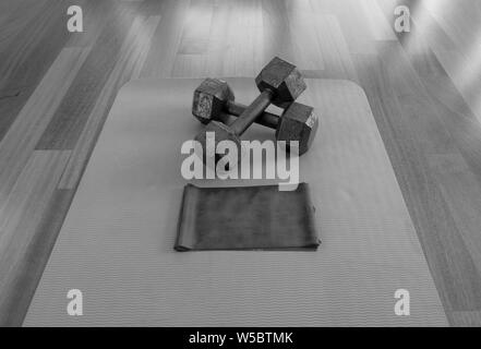 Versione in bianco e nero di attraversata manubri e banda di esercizio su un materassino yoga per un allenamento domestico Foto Stock