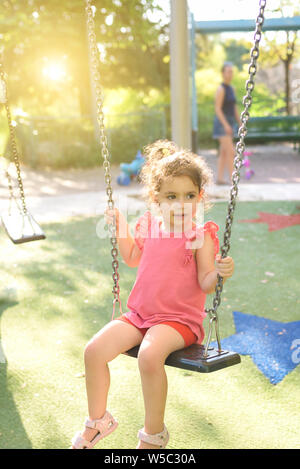 Bambino felice ragazza ridere ed oscillante su un altalena presso il parco giochi di estate. Foto Stock