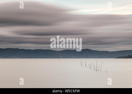 Bella lunga esposizione vista del lago Trasimeno (Umbria, Italia), ancora con acqua e nuvole in movimento Foto Stock