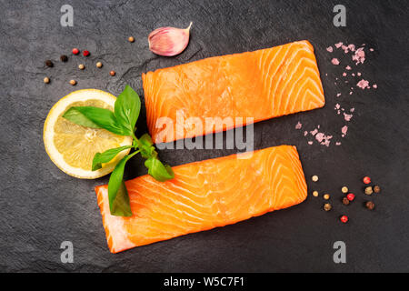 Due fette di crudo fresco salmone con sale, pepe, aglio, basilico e limone, girato dalla parte superiore su uno sfondo nero Foto Stock