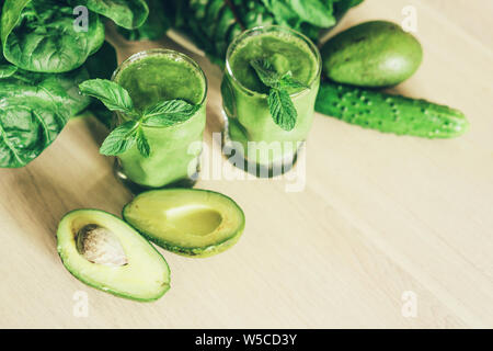 Su un tavolo di legno ci sono 2 bicchieri con un frullato verde preparato di fresco e ingredienti per cucinare Foto Stock