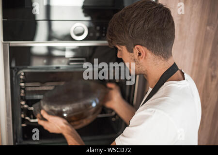 Sorridente giovane uomo in fase di riscaldamento la cena nella sua cucina Foto Stock