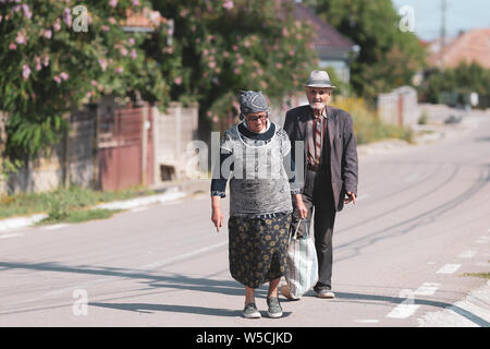 Bontida, Romania - 21 Luglio 2019: una coppia di anziani su una strada vuota in un villaggio rurale in Romania su un luminoso caldo giorno d'estate Foto Stock