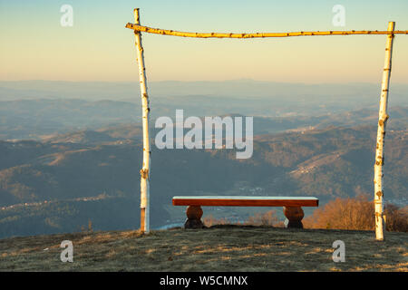 Panca in legno. Attorno ad esso è in legno a telaio di betulla. Il paesaggio della Slovenia al sunrise. La foto è stata scattata dalla cima della lisca hill Foto Stock