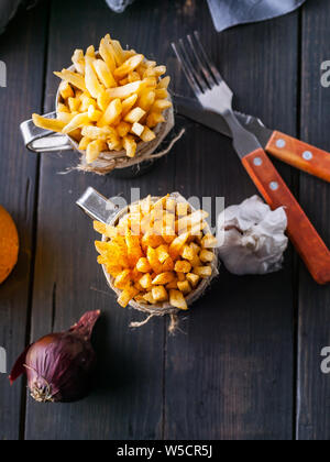 Le patate fritte fatte in casa, la cipolla, l'aglio, il cucchiaio e forchetta scuro su un tavolo di legno. Colpo verticale Foto Stock