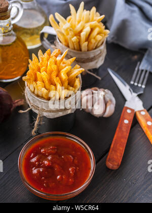 Le patate fritte fatte in casa, cipolla, aglio, salsa di pomodoro, Cucchiaio e forchetta scuro su un tavolo di legno. Colpo verticale Foto Stock