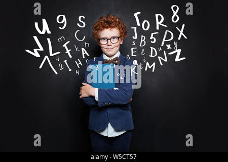 Scuola ragazzo in blu uniforme dello studente con libro su sfondo blackboard Foto Stock