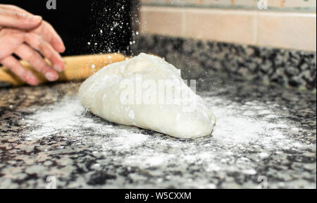 Lo Chef versando la farina sulla pasta per cucinare una ricetta casalinga. La preparazione e gli impasti per la cottura del pane o la pizza a casa con spazio copia a destra. Foto Stock