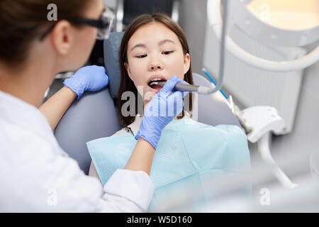 Ritratto di giovane donna asiatica giacente in poltrona odontoiatrica durante la procedura medica, spazio di copia Foto Stock