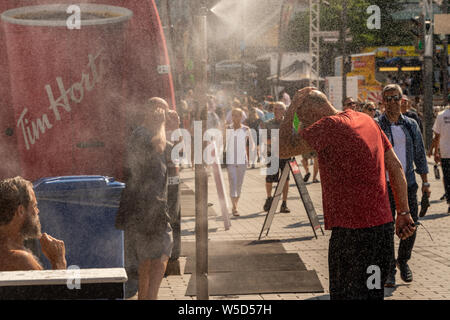 Montreal, CA - 27 Luglio 2019: la gente camminare sotto sistema di appannamento di raffreddarsi (nebbia sistema di raffreddamento) durante l'ondata di caldo nel Quartier des festivals. Foto Stock