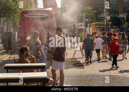 Montreal, CA - 27 Luglio 2019: la gente camminare sotto sistema di appannamento di raffreddarsi (nebbia sistema di raffreddamento) durante l'ondata di caldo nel Quartier des festivals. Foto Stock