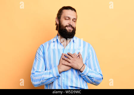 Romantico emotivo amare l uomo con gli occhi chiusi in elegante Camicia a Righe toccando il suo cuore , è caduto nell'amore, forte sensazione. Foto Stock