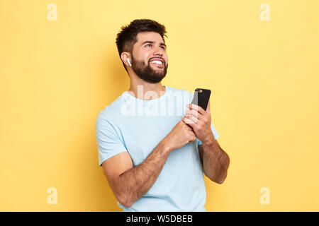 Giovane uomo attraente azienda smart phone e ascolto di radio. close up vista laterale foto tempo libero. studio shot Foto Stock