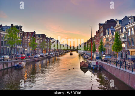 Edifici, alberi e barche lungo il canale al tramonto il tempo in Amsterdam, Paesi Bassi Foto Stock