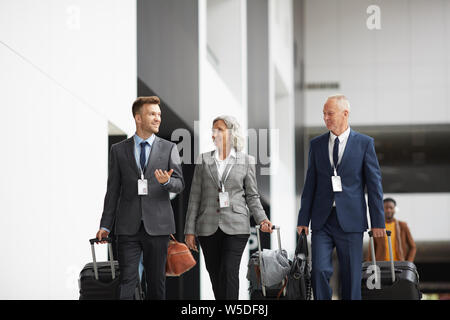 Gruppo di certi dirigenti d' azienda in giacca a piedi con i bagagli in aeroporto e discutere di affari Foto Stock