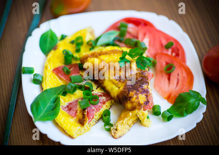 Frittata fritte fatte in casa dalle uova organiche con i pomodori e le cipolle verdi su uno sfondo di legno Foto Stock