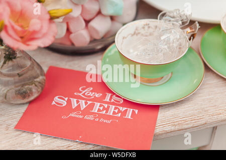 Primo piano di una tazza con dolci su uno sfondo di un vaso con marshmallows e una scheda con le parole di amore è dolce, il fuoco selettivo Foto Stock