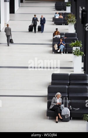 Al di sopra di vista business persone sedute e passeggiate in aeroporto moderno sala di attesa Foto Stock