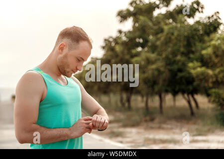 Ritratto di ragazzo caucasico in azzurro t-shirt guardando fitness letture tracker prima o dopo il jogging. Foto Stock