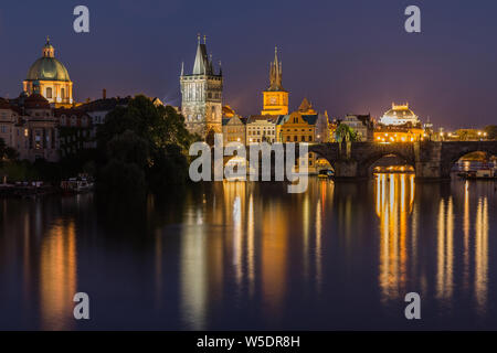 Ponte Carlo di notte a Praga. Torre e ponte storico in pietra sopra la Moldava con illuminazione tra la città vecchia e la città minore. Riflessioni Foto Stock