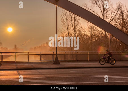 Vista attraverso un ponte di prua un tramonto su un canale a Berlino in una nebbiosa mattina con la luce del sole da favola. Sul lato destro si può vedere un ciclista. Foto Stock