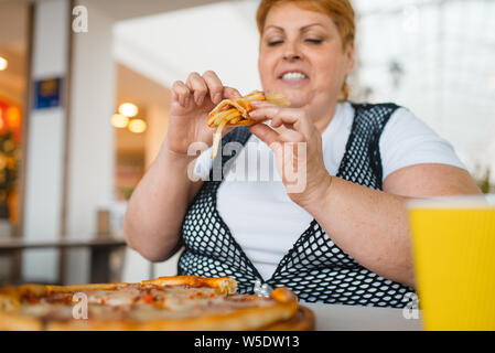 La donna grassa mangiare la pizza con le patatine fritte Foto Stock