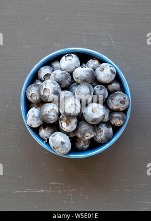 Mature di mirtilli organico in una ciotola blu sulla superficie nera, vista dall'alto. Estate Berry. Piatto, laici overhead, dall'alto. Foto Stock