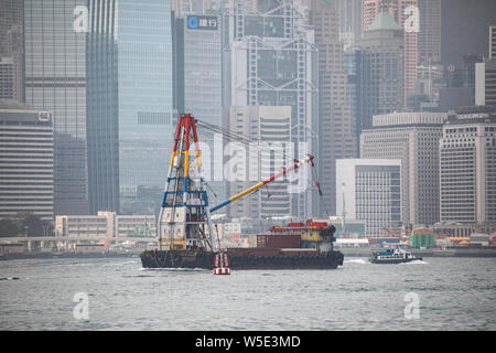 Contenitore con chiatta derrick nel Porto Victoria, Isola di Hong Kong grattacieli sullo sfondo Foto Stock