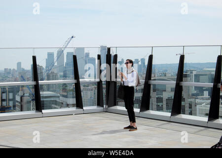 Donna con telefono cellulare telecamera in piedi sul tetto giardino terrazza 120 Fenchurch Street edificio vista di Canary Wharf dalla città Di Londra UK KATHY DEWITT Foto Stock