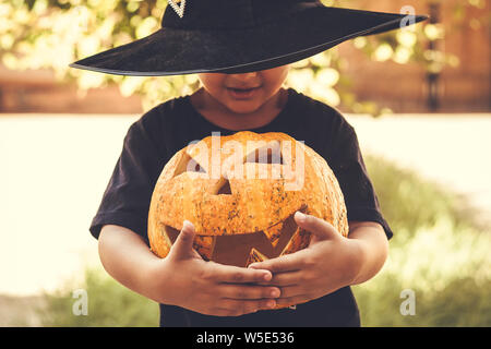 Halloween 2019. Little Boy holding scolpito zucca di Halloween - Jack O'lanterne a all'esterno. Famiglia i preparativi per Halloween holiday. Foto Stock