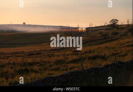 2 DB Cargo classe 66 locomotive diesel passando di Shap Wells sulla costa ovest mainline in Cumbria con un treno merci che trasportano la calce al tramonto Foto Stock