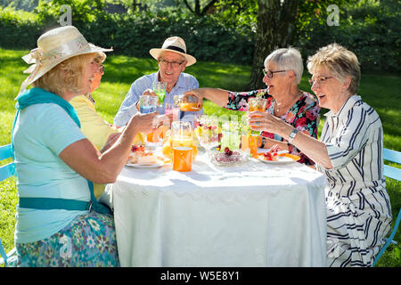 Alti membri della famiglia pic-nic, seduti attorno al tavolo e di bere succo di arancia e mangiare la torta di frutta, una donna serve succhi di frutta a quattro amici. Foto Stock