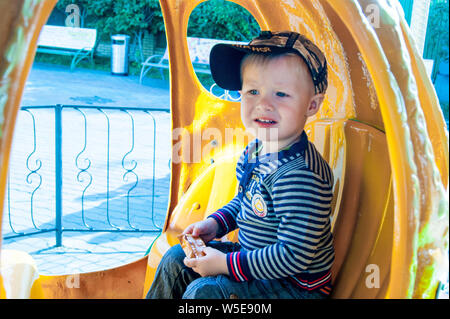 Una tre-anno-vecchio biondo e con gli occhi azzurri ragazzo corse merry-go-round in una zucca gialla. Divertimento, attività, impressioni, emozioni. Il freddo di estate o inizio autunno Foto Stock