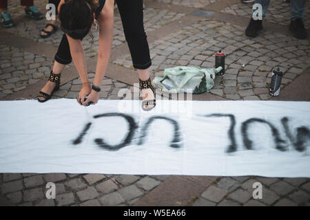 Dettagli con le mani di una giovane donna di scrittura con una vernice nera spray un messaggio femminista su un pezzo di stoffa whitee Foto Stock