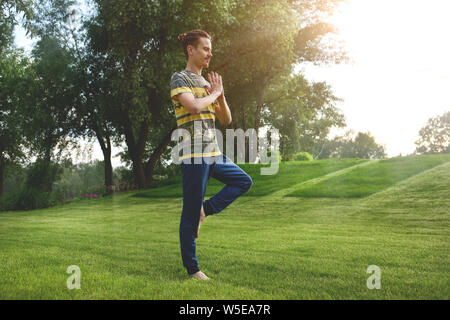 Uomo Fitness Ginnastica su una gamba isolata nel parco. Godersi la natura, lo yoga e la meditazione concetto. pratiche spirituali. Foto Stock