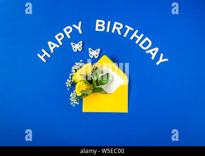 Rose di colore giallo e bianco Gypsophila in busta close-up su sfondo blu. Testo Happy Birthday, bianco farfalle. Vista superiore, piatto laici. Modello per bi Foto Stock