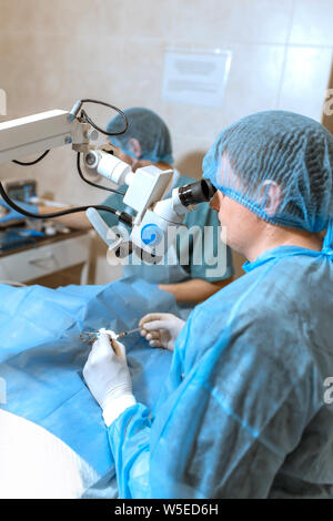 Oculista chirurgo guardando attraverso il microscopio chirurgico facendo operazione difficoltosa. Foto Stock