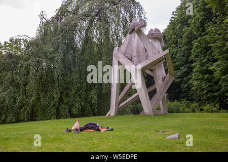 Senzatetto Uomo nel Parco Sempione a Milano accanto a una scultura. Foto Stock