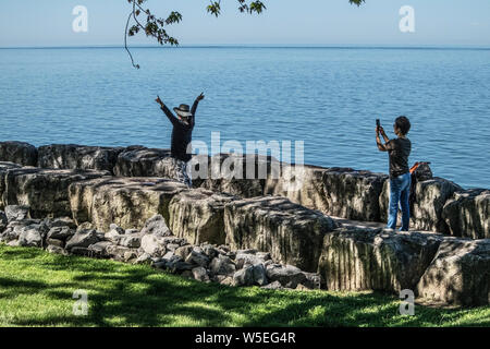 Sul sentiero del Lago Ontario a Niagara sul lago, due giovani donne asiatiche. Uno prende l'immagine dell'altro. Lei prende funny pone.. Foto Stock